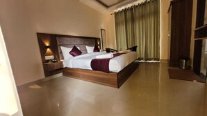 A spacious hotel room with a large bed, a nightstand, a mirror, and a view of the outside through a window with curtains.
