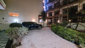 A paved pathway leading to a building with a parked car. There are potted plants along the path.