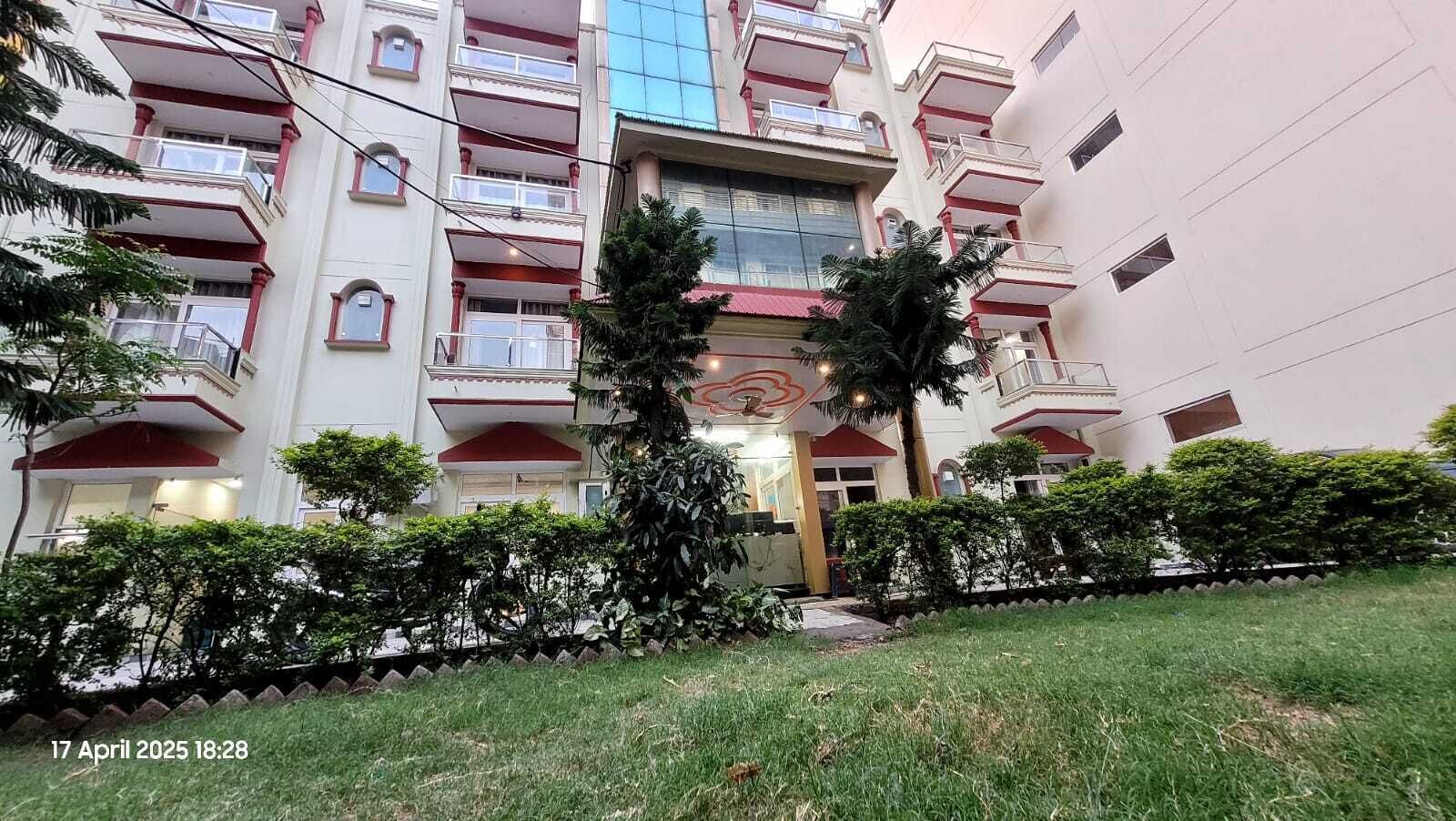 Un immeuble à plusieurs étages, doté de balcons, d’une entrée centrale et entouré de verdure.