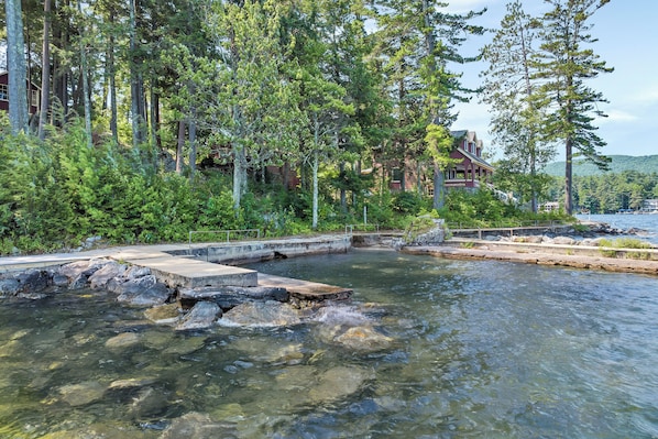 A clear river with rocks, surrounded by dense trees and a wooden dock.