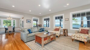 A spacious living room with hardwood flooring, a grey sofa, a wooden coffee table, and patterned armchairs. - Lake Winnipesauke sleeps 9 with stunning sunset views (Alton Bay)