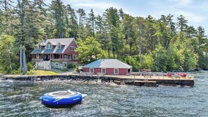 A house by a lake with a dock and a blue inflatable boat. - Lake Winnipesauke sleeps 9 with stunning sunset views (Alton Bay)