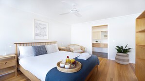 A modern hotel room with a large bed, a bedside table, a chair, a small bathroom, and a ceiling fan. - Buwarla House – pet friendly beach house (Currarong)