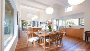 Una cocina amplia con suelo de madera, una zona de comedor con mesa y sillas, y ventanas grandes que aportan luz natural.