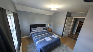 A bedroom with a bed, a nightstand, a lamp, and a door leading to another room.