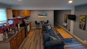 A compact living space with a kitchenette, a sofa, a small dining table, and a TV mounted on the wall.