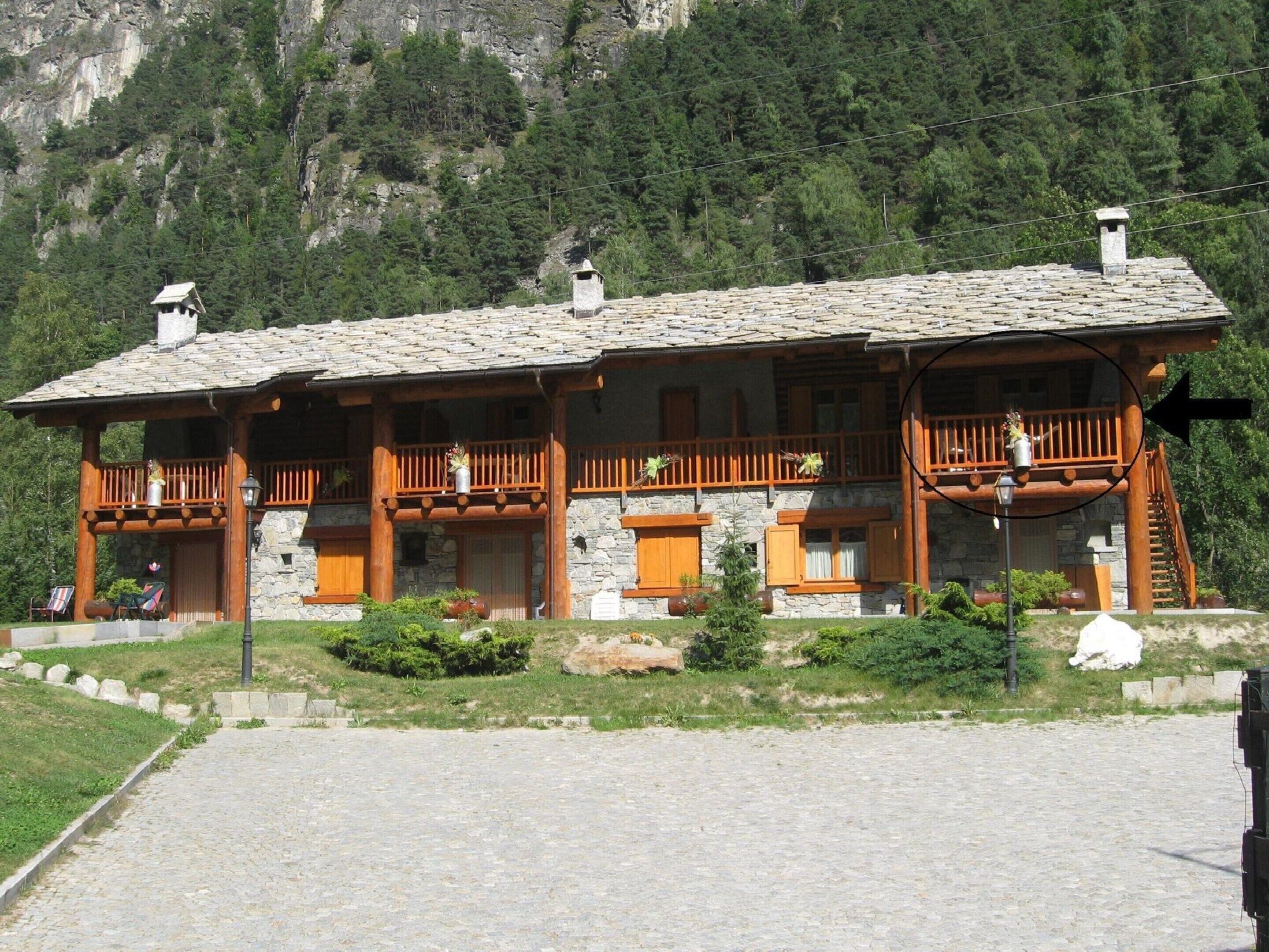 Un edificio de estilo chalet con fachada de piedra, balcones de madera y una escalera de piedra que lleva a los pisos superiores.
