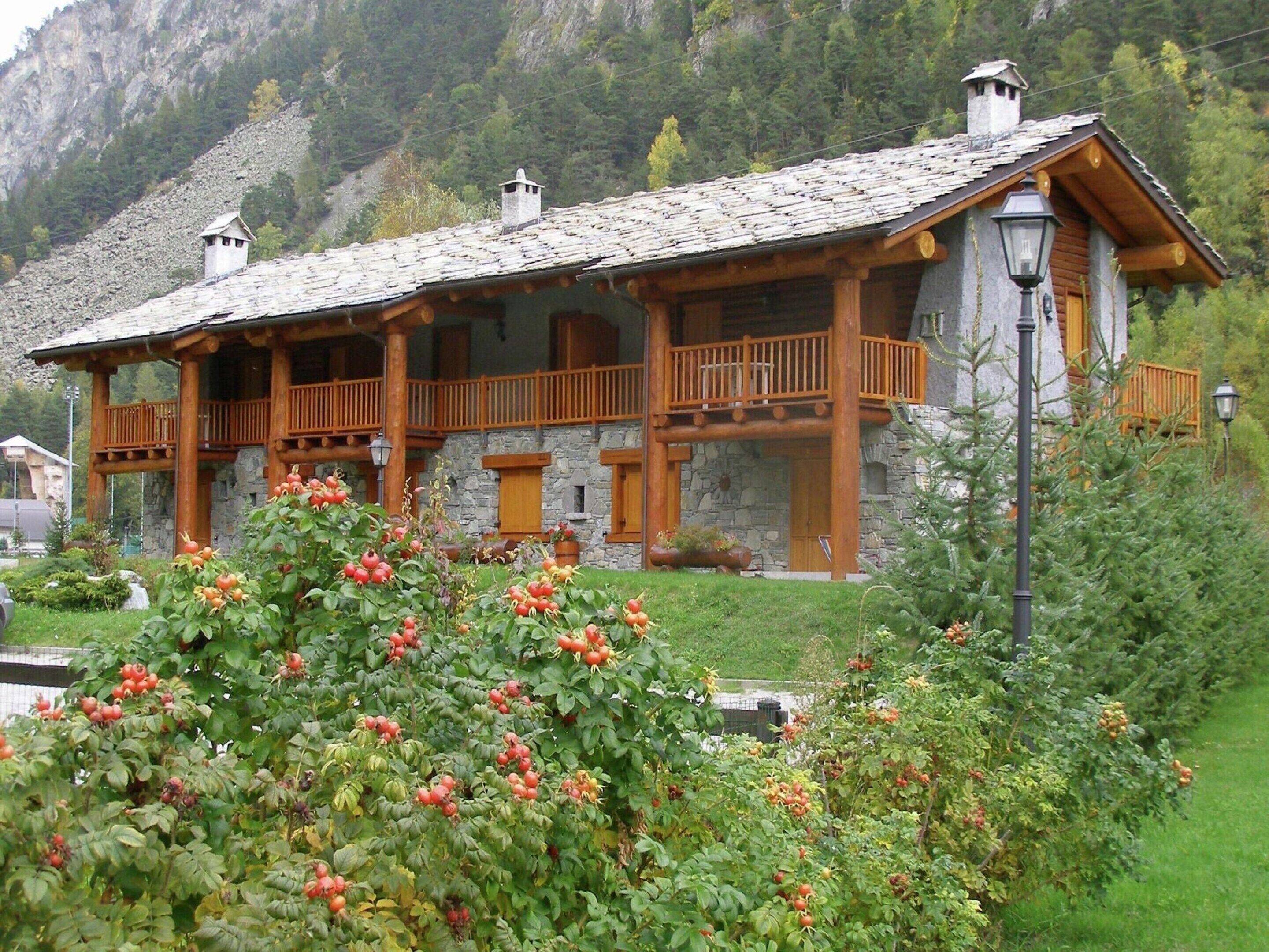 Un bâtiment de style chalet, doté d’une façade en pierre, de balcons en bois et d’une cheminée en pierre.