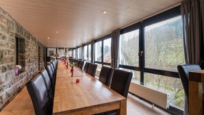 A long wooden table with black leather chairs in a room with stone walls and large windows. - Exclusive Group House in Winterberg in the Forest (Winterberg)