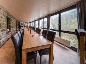 A long wooden table with black leather chairs in a room with stone walls and large windows. - Exclusive Group House in Winterberg in the Forest (Winterberg)
