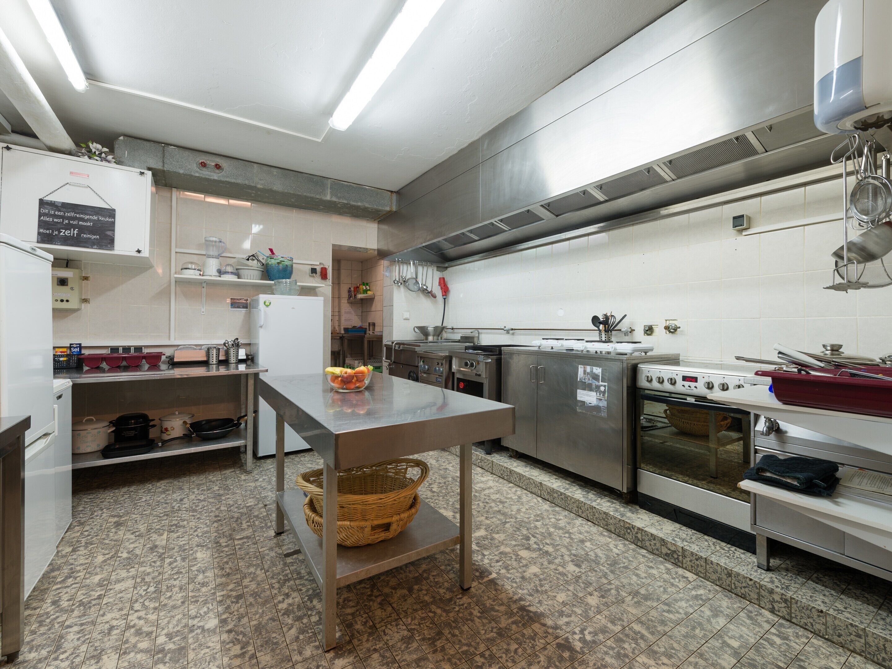 A commercial kitchen with stainless steel appliances, a large table, and a tiled floor.