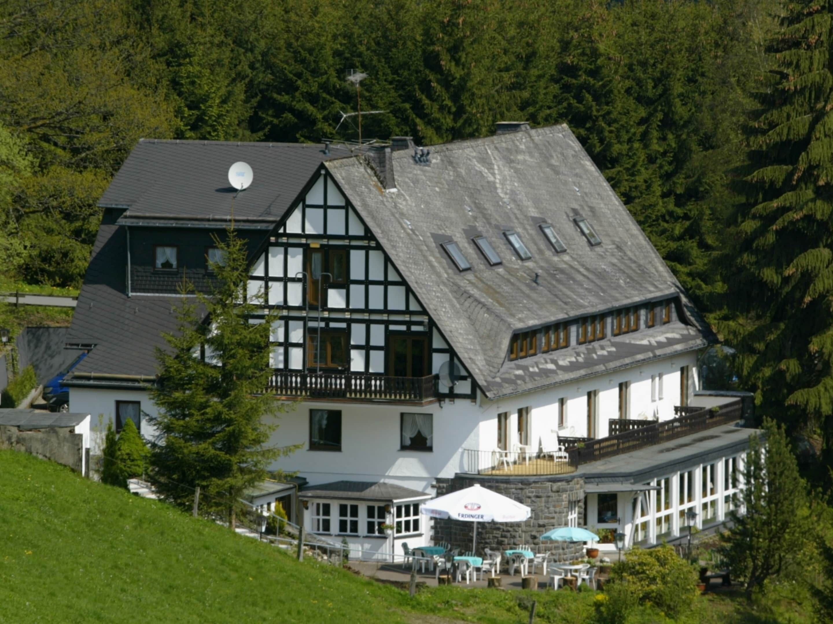 A traditional chalet-style building with a steeply pitched roof, a balcony, and a terrace with outdoor seating.