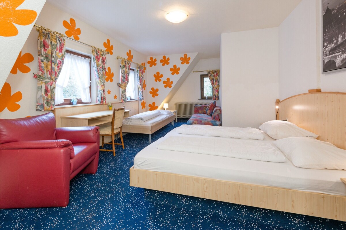 A bedroom with a bed, a desk, a chair, and a red sofa.