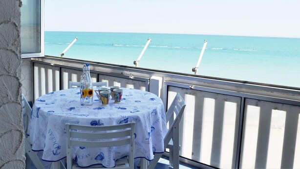 A table with a blue tablecloth and a bottle of orange juice, overlooking a calm sea with a clear sky. - Welcoming Apartment in Marotta at the Seabeach (Mondolfo)