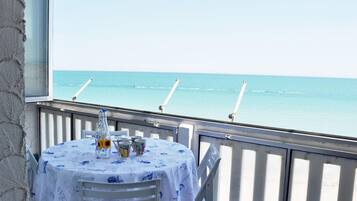 A table with a blue tablecloth and a bottle of orange juice, overlooking a calm sea with a clear sky.