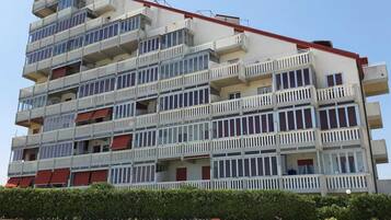 A multi-story building with balconies, a red roof, and a gravel ground.