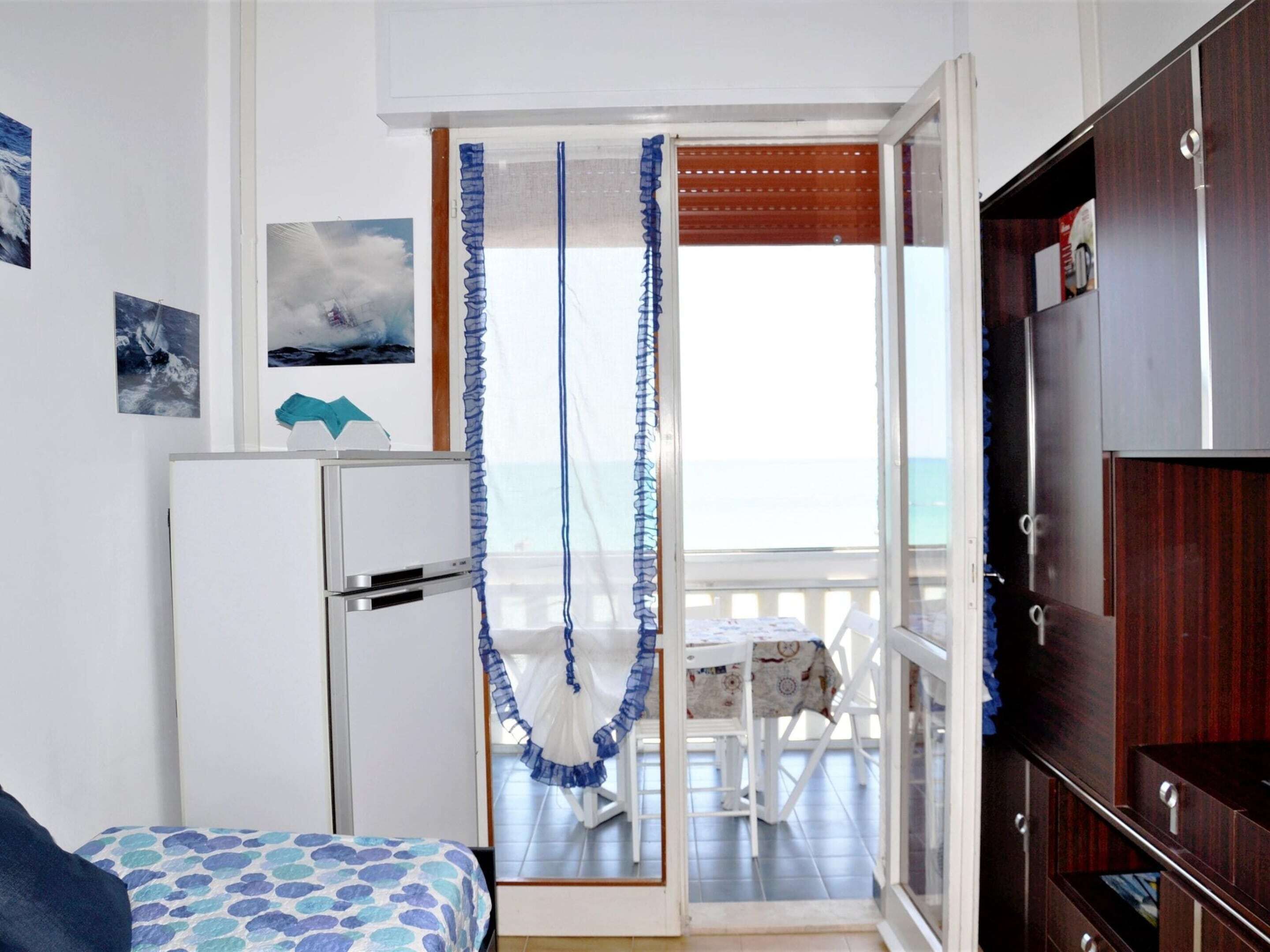 A room with a bed, a small table, and a view of the sea through an open door.