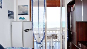 A room with a bed, a small table, and a view of the sea through an open door. - Welcoming Apartment in Marotta at the Seabeach (Mondolfo)