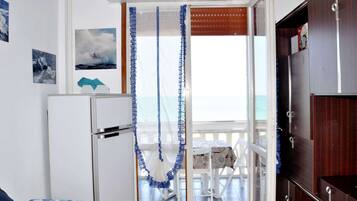 A room with a bed, a small table, and a view of the sea through an open door.