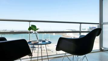 A balcony with two black chairs, a small round table with a glass vase and two glasses, and a view of a body of water and buildings.