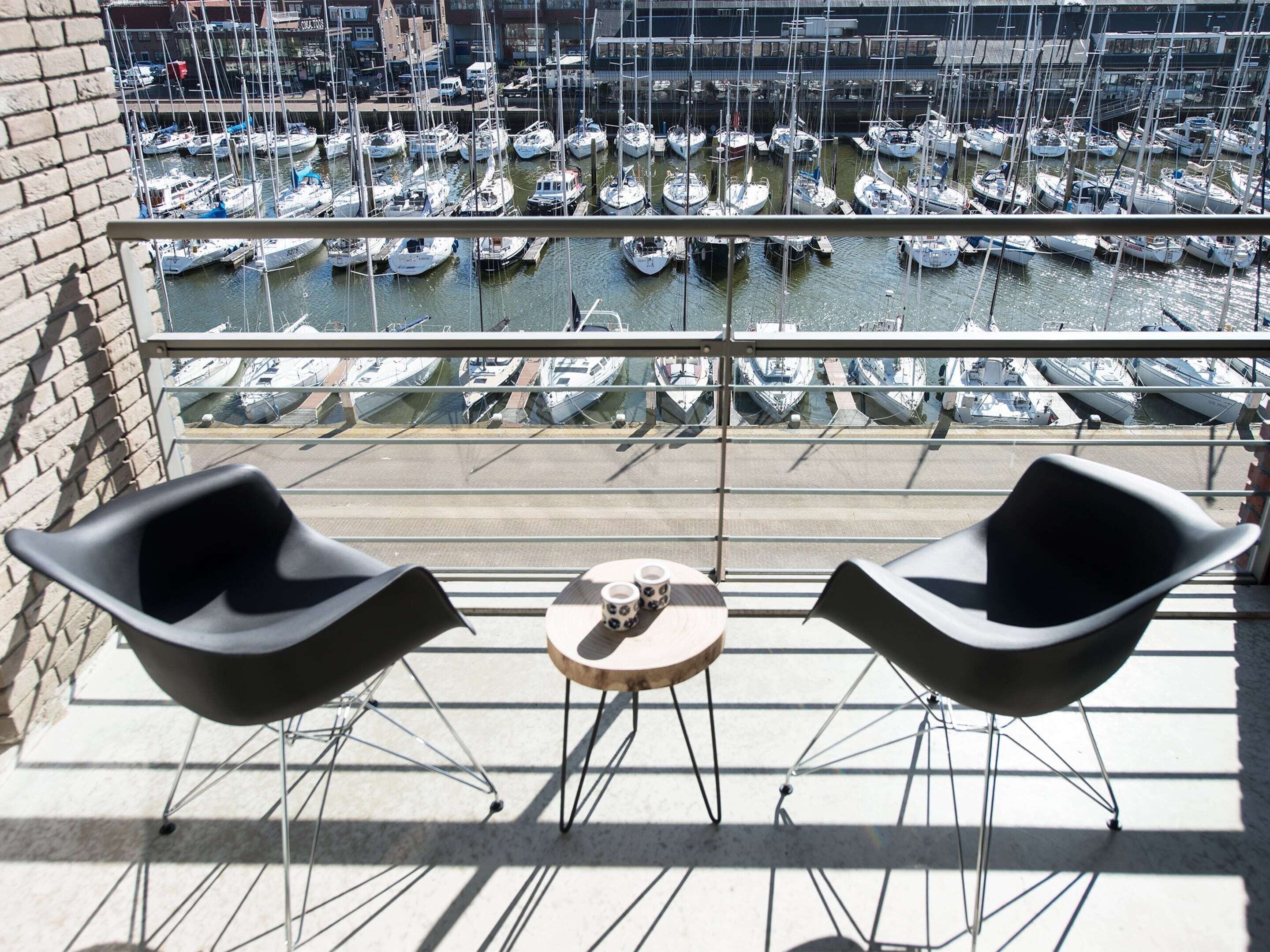 A balcony with two black chairs and a small table, overlooking a marina with numerous boats docked.