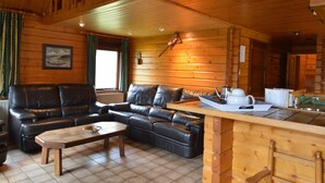 A cozy cabin interior with a leather sofa, a wooden dining table, and a kitchen area with a sink and countertop. - Comfortable Chalet in Ovifat Near Ski Lift (Waimes)
