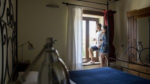 Un dormitorio con cama, lámpara de noche, ventana con cortinas y techo de madera.