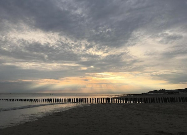 Une plage avec une jetée en bois qui s’avance dans l’eau, un ciel nuageux et un coucher de soleil.