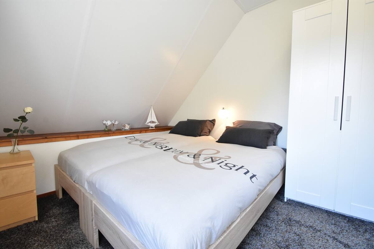 Een slaapkamer met een bed, een nachtkastje, een dressoir, een kledingkast en een wandplank met decoratieve objecten.