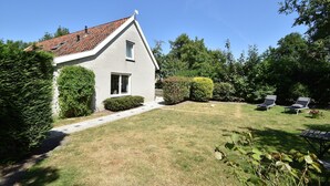 A house with a sloped roof, a front door, and a small window. There is a lawn with a pathway leading to the house, and two lounge chairs in the yard. - Cozy Holiday Home in Zonnemaire Near Lakebeach (Zonnemaire)