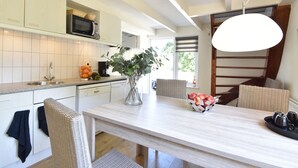 Eine moderne Küche mit weißen Schränken, einer Edelstahl-Spüle, einer Mikrowelle und einem Essbereich mit einem hellen Holztisch und Korbstühlen.