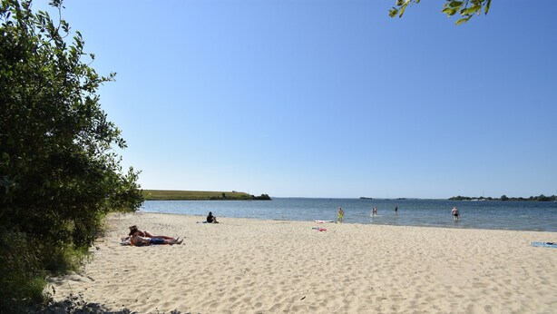 Ein Sandstrand mit badenden und sonnenden Menschen.