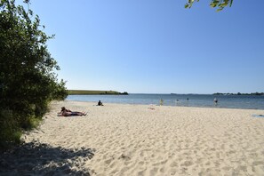 A sandy beach with people sunbathing and swimming. - Cozy Holiday Home in Zonnemaire Near Lakebeach (Zonnemaire)
