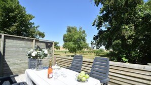 An outdoor dining area with a table set for two, a bottle of wine, and a bowl of apples. - Cozy Holiday Home in Zonnemaire Near Lakebeach (Zonnemaire)
