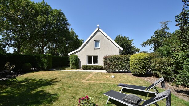 A house with a triangular roof, a small window, and a door. There is a lawn with two lounge chairs and a potted plant. - Cozy Holiday Home in Zonnemaire Near Lakebeach (Zonnemaire)
