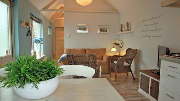 A cozy living room with a white sofa, wicker chairs, a large white table with a plant, and a TV on a wooden cabinet. - Holiday Home in Egmond aan zee With Fenced Garden (Egmond aan Zee)