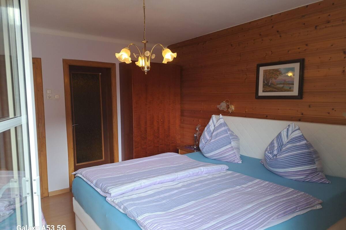A bedroom with a bed, wooden panel walls, a chandelier, and a framed picture on the wall.