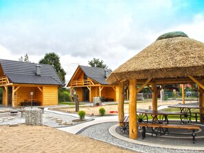 Un edificio in stile baita di legno con un padiglione a tetto di paglia, circondato da vialetti ghiaiosi e tavoli da picnic.