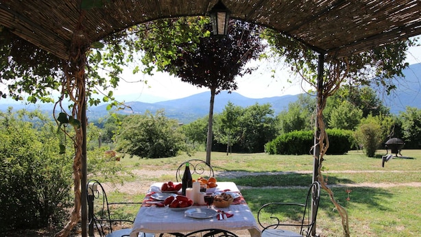An outdoor dining area with a table set for two, surrounded by metal chairs, under a thatched roof. - Farmhouse With Swimming Pool in Casperia (Casperia)