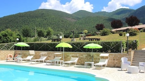A swimming pool with lounge chairs and umbrellas, surrounded by stone walls and a view of green hills. - Farmhouse With Swimming Pool in Casperia (Casperia)