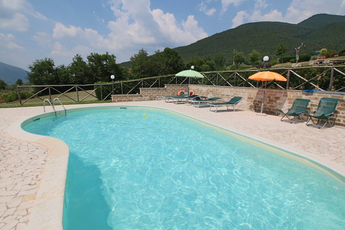 Une piscine à bordures courbes, entourée de chaises longues et de parasols, avec une chaîne de montagnes en toile de fond.