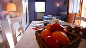 A room with a dining table set for two, a basket of fruit, and a bed with a blue bedspread. - Farmhouse With Swimming Pool in Casperia (Casperia)