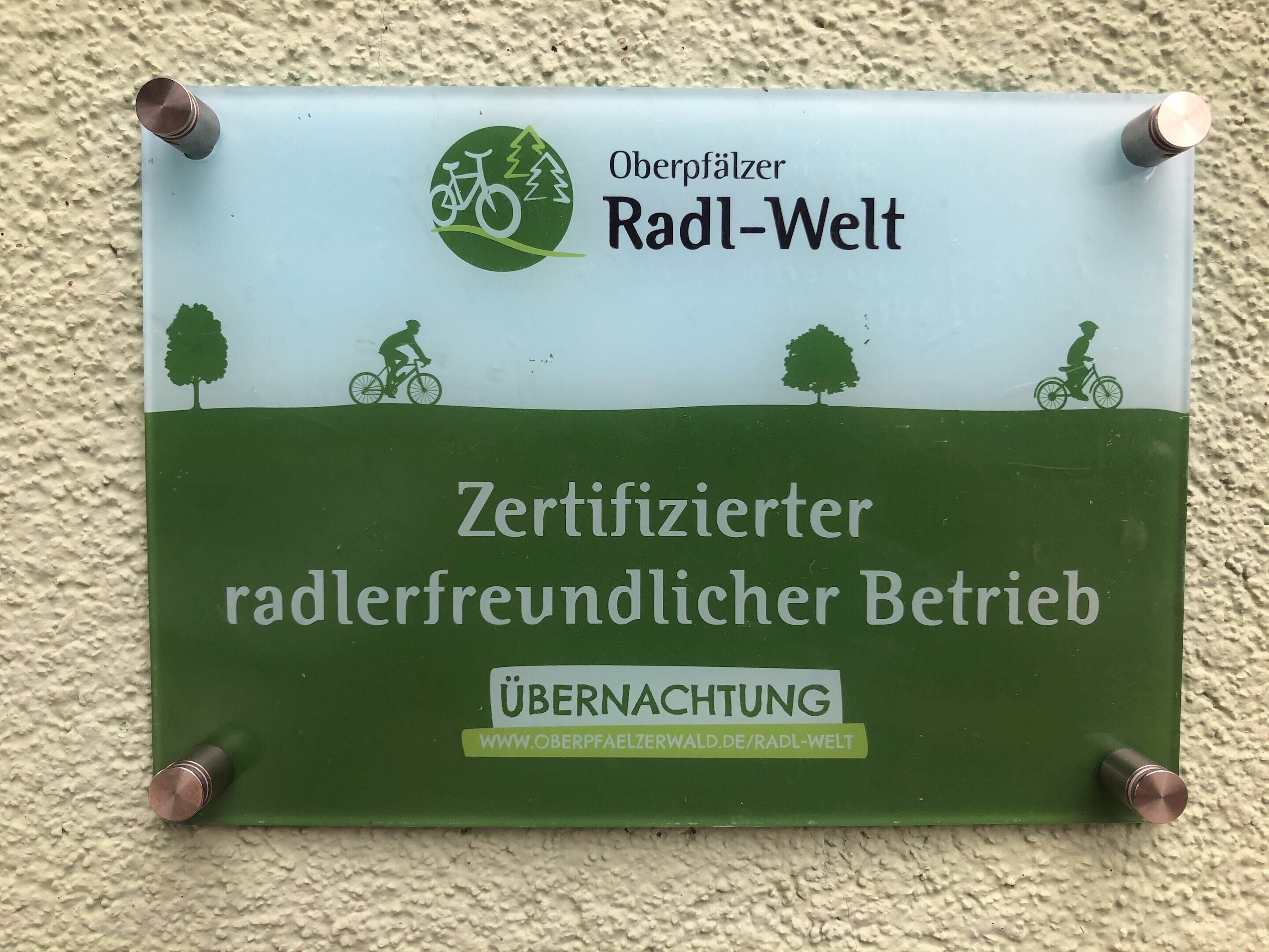 A signboard with a green and white design, featuring a bicycle and trees, and text in German.
