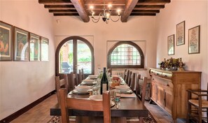A dining area with a long wooden table set for a meal, flanked by two arched windows.