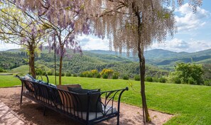 A bench with cushions under a tree with hanging flowers, overlooking a green valley and hills. - Beautiful Villa in San Giovanni del Pantano With Pool (Perugia)
