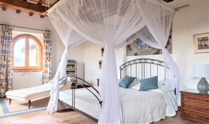A bedroom with a four-poster canopy bed, a small sofa, a wooden dresser, and a bookshelf.