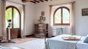 A bedroom with a bed, a dresser, a telescope, and two windows with curtains. - Beautiful Villa in San Giovanni del Pantano With Pool (Perugia)