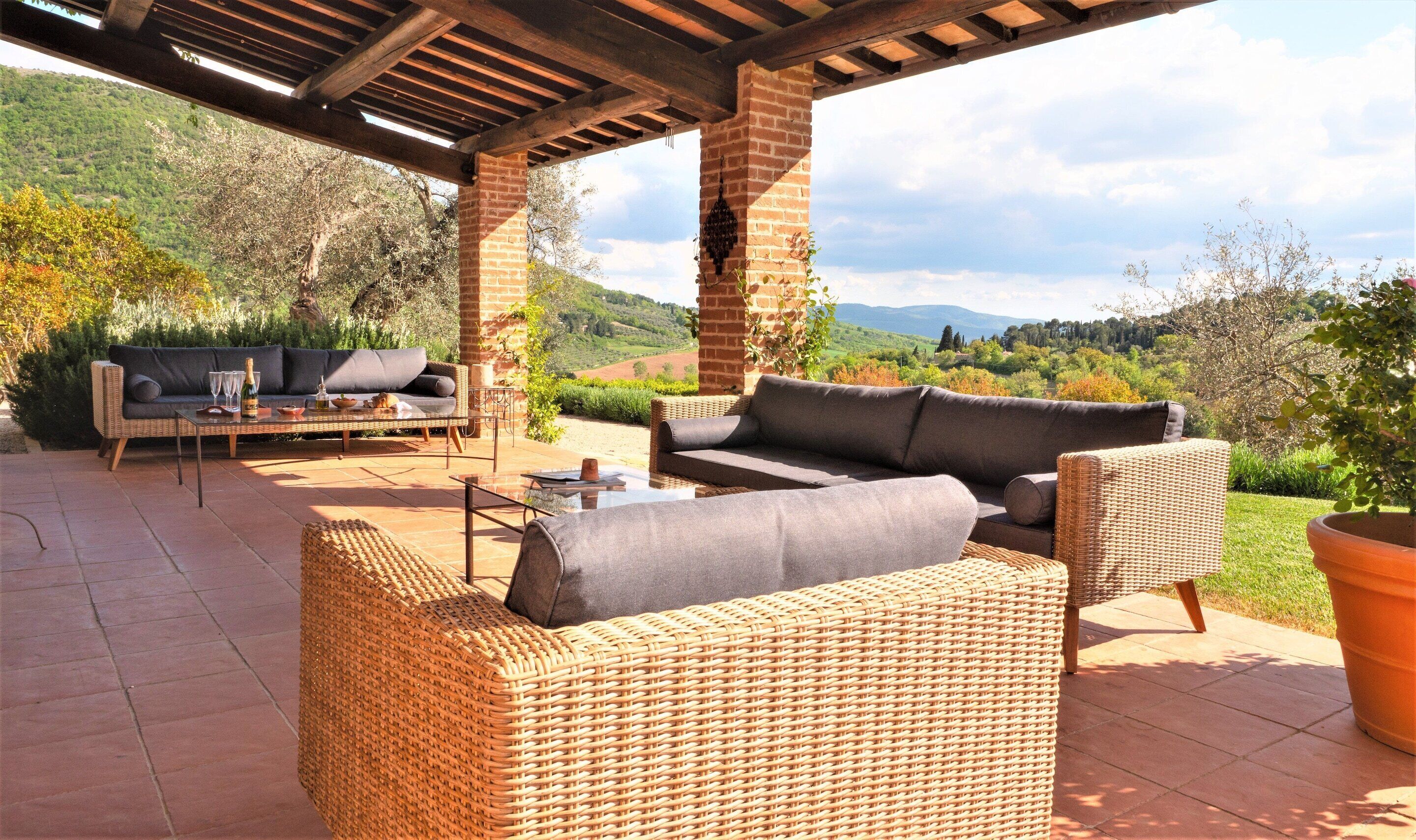 An outdoor patio with wicker furniture, a brick wall, and a view of the countryside.