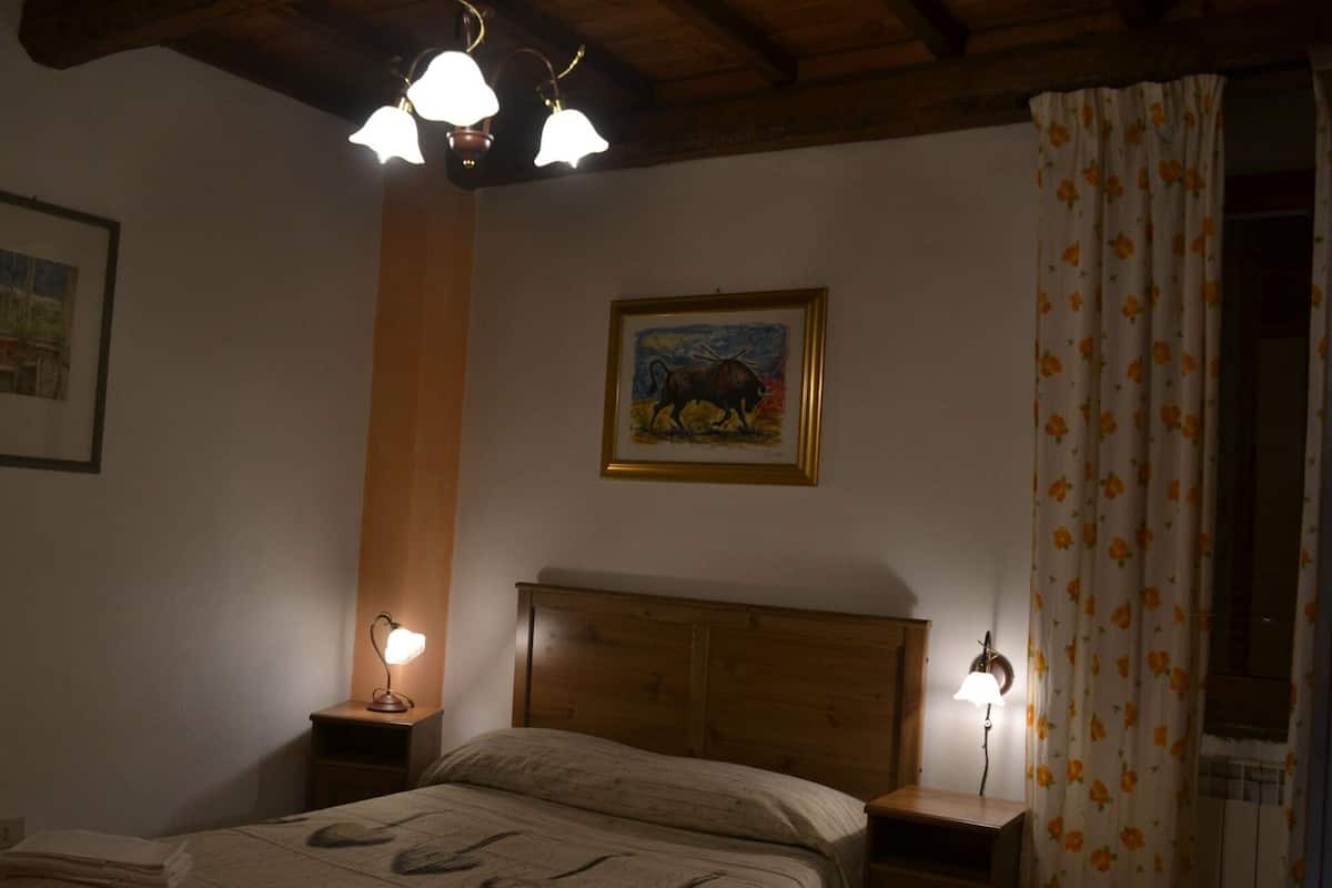 Ein Schlafzimmer mit einem hölzernen Kopfstück, einem Gemälde von Stieren, zwei Nachttischlampen und einem blumigen Vorhang.