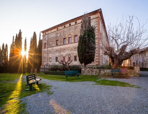 A historic building with a gravel courtyard, benches, and a tree. - Lovely Farmhouse in Monticiano With Garden (Monticiano)